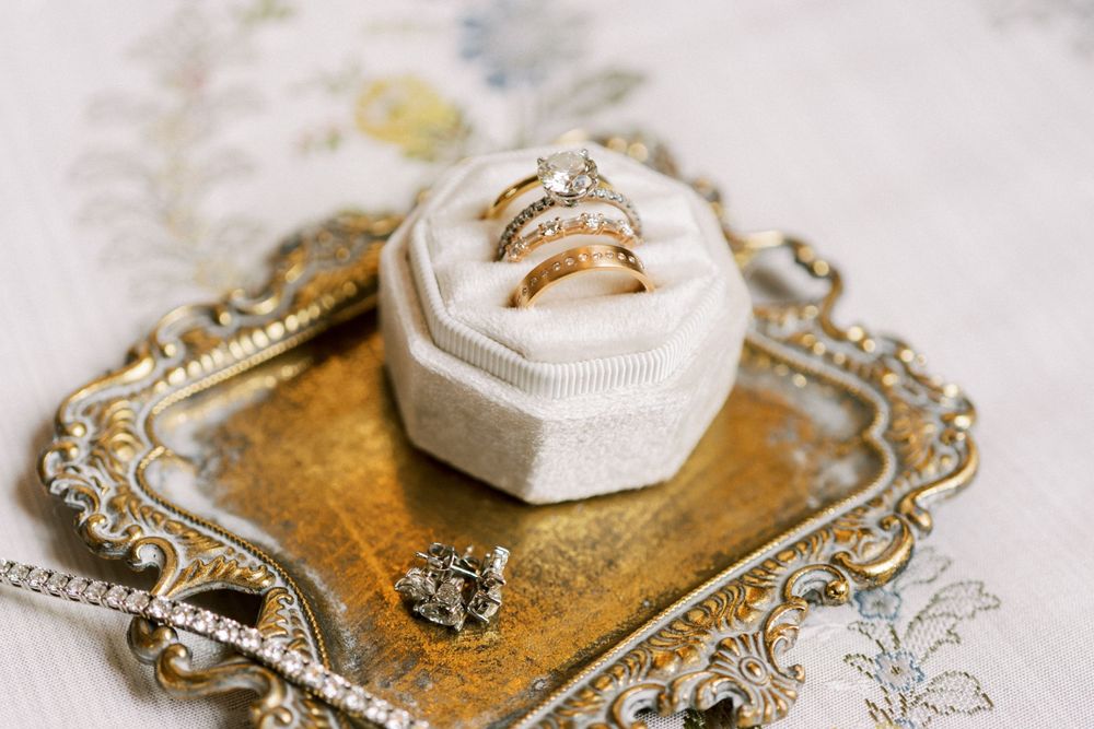 Vintage gold decorative trays with wedding rings and jewelry displayed on white linen.