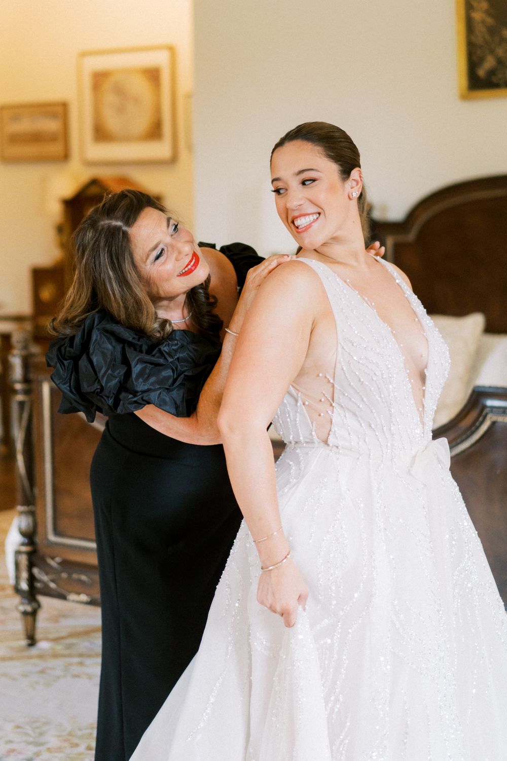 Two people share joyful embraces in black and white bridesmaid dresses at an elegant indoor venue.