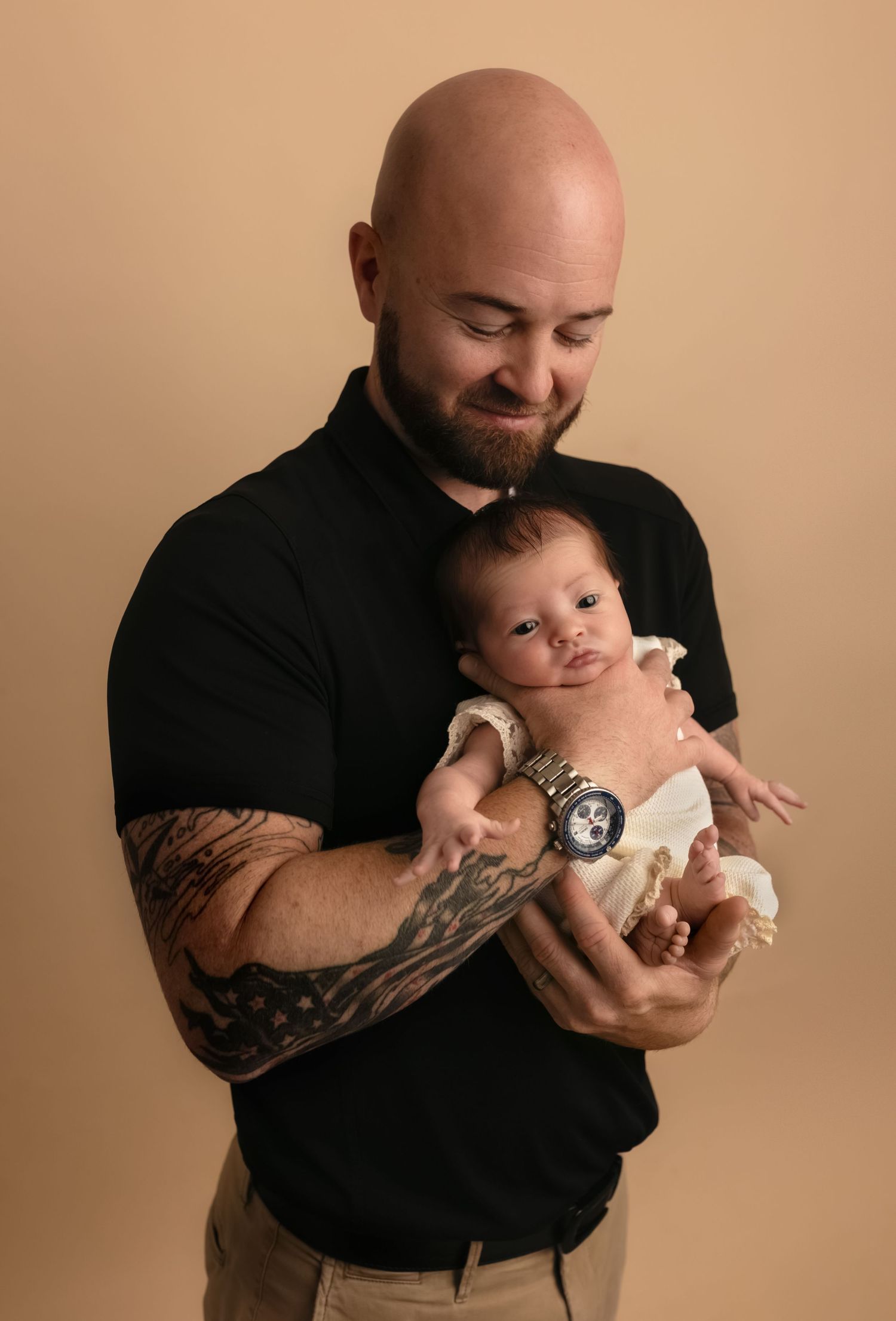 Proud dad with patriotic tattoos lovingly holds his baby daughter, captured by Somerset Portraits, a Charlottesville newborn photographer.
