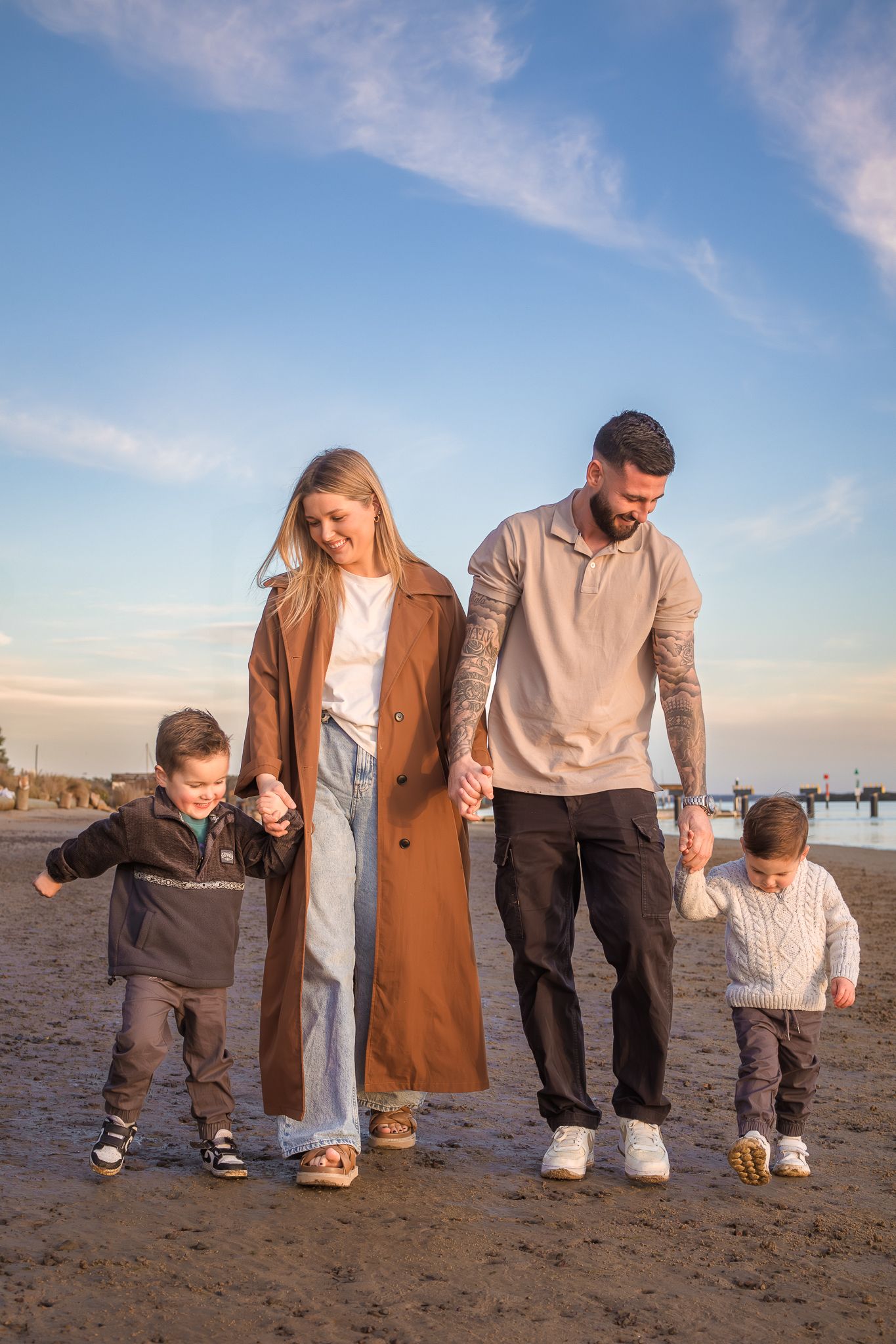 Young couple with two toddler boys hand in hand on a muddy beach.