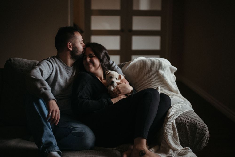 A couple relaxes together on a cozy couch in a dimly lit room with soft shadows and warm ambiance.