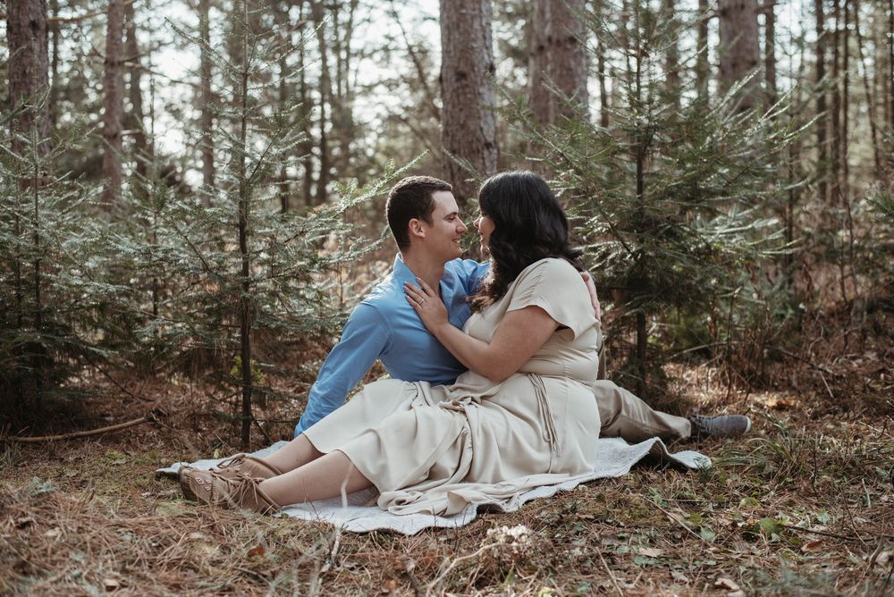 A romantic couple sits on a blanket sharing an intimate moment in a serene forest setting.