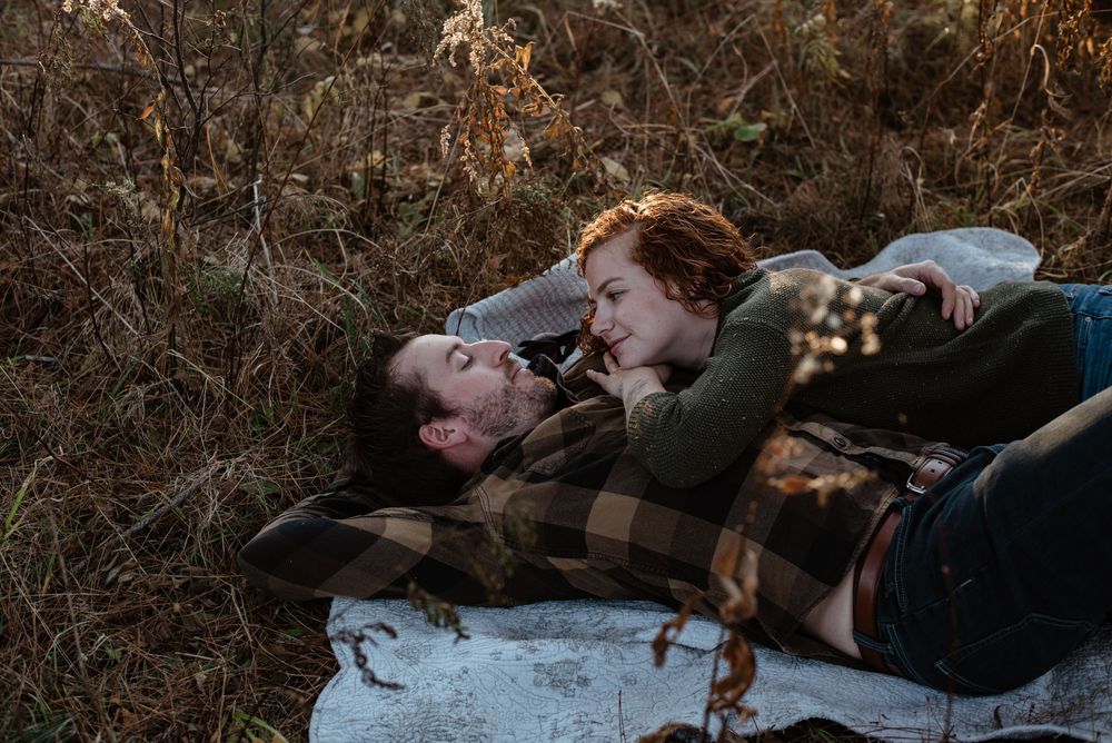 Two people laying down together peacefully in a field of dried autumn grass.