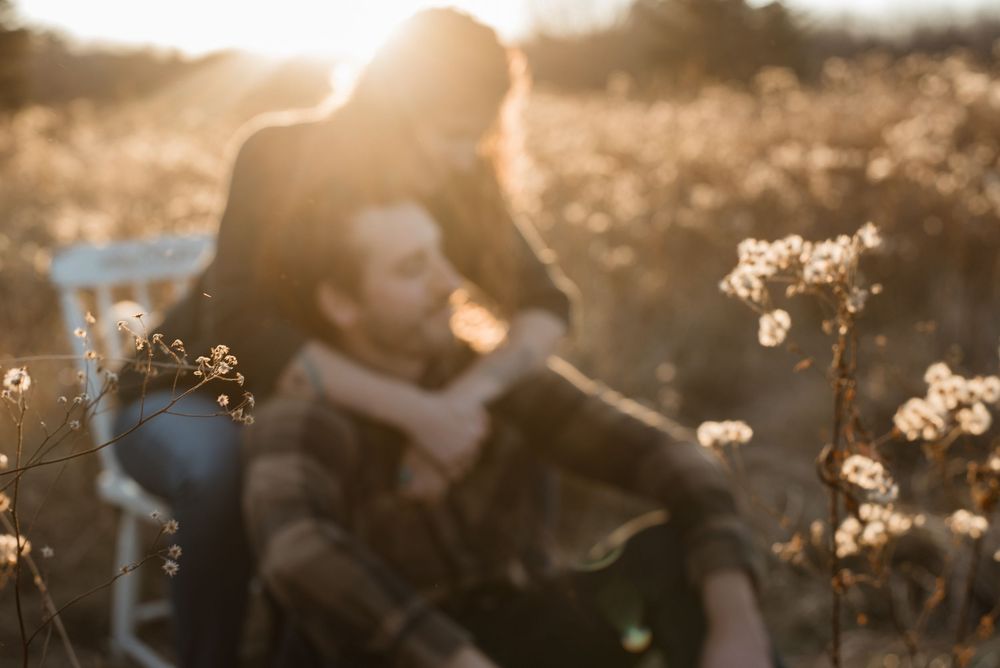 A couple shares a romantic moment in a golden field at sunset with backlit flowers creating a dreamy atmosphere.
