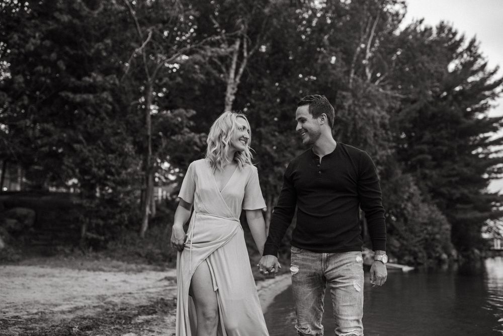 A couple walks together holding hands by a lakeside in a black and white photo.