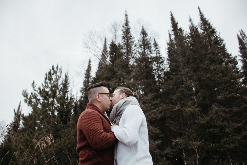 An elderly couple embracing outdoors against a backdrop of evergreen trees.