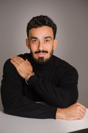 Creative headshots of man with beard wearing black sweater against neutral background.