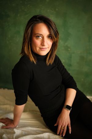 Professional portraits in black turtleneck against textured green background.