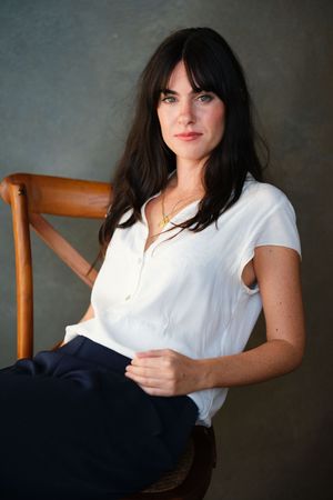 Casual portraits in white sleeveless top while seated on wooden chair.