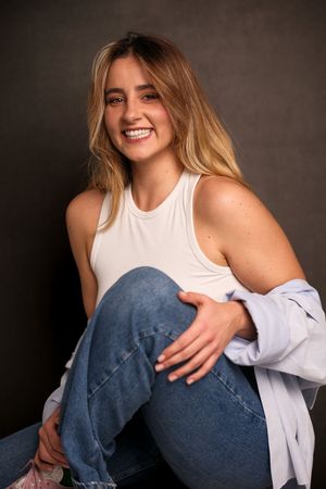 Casual portrait series of person in white tank top and jeans against dark backdrop.