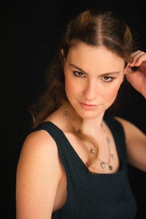 Artistic portrait series in dark lighting featuring delicate jewelry and patterned top.