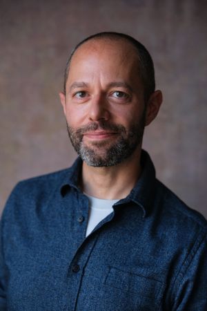 Professional headshot series of person in blue denim shirt with neat beard against neutral backdrop.