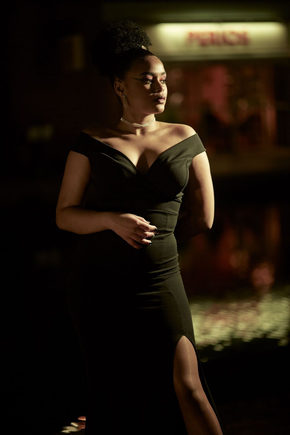 Dramatic low-light portrait in black evening dress with theatrical spotlight effect.