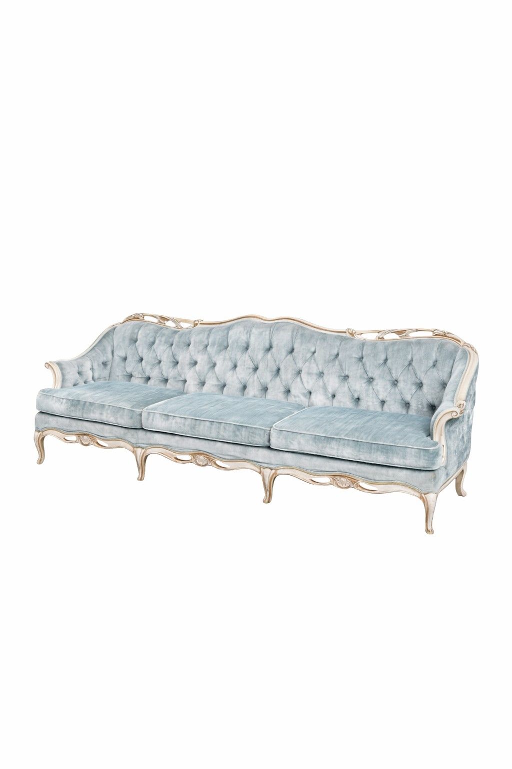 A vintage blue tufted velvet sofa sits outdoors on grass against a backdrop of lush green trees and foliage.
