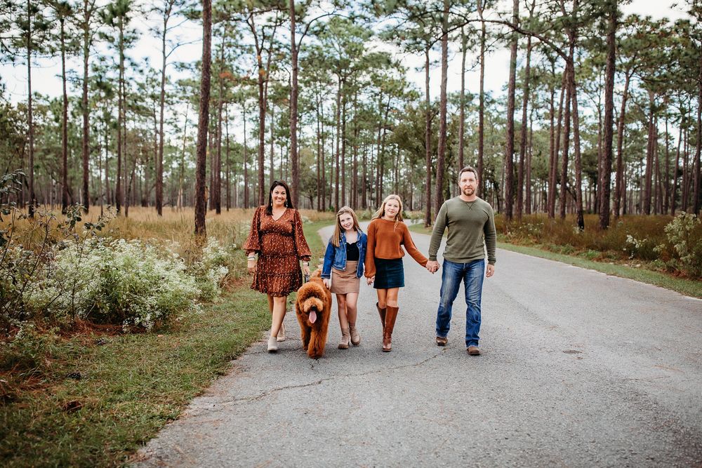 A family walks together on a winding path through a serene pine forest during golden hour.