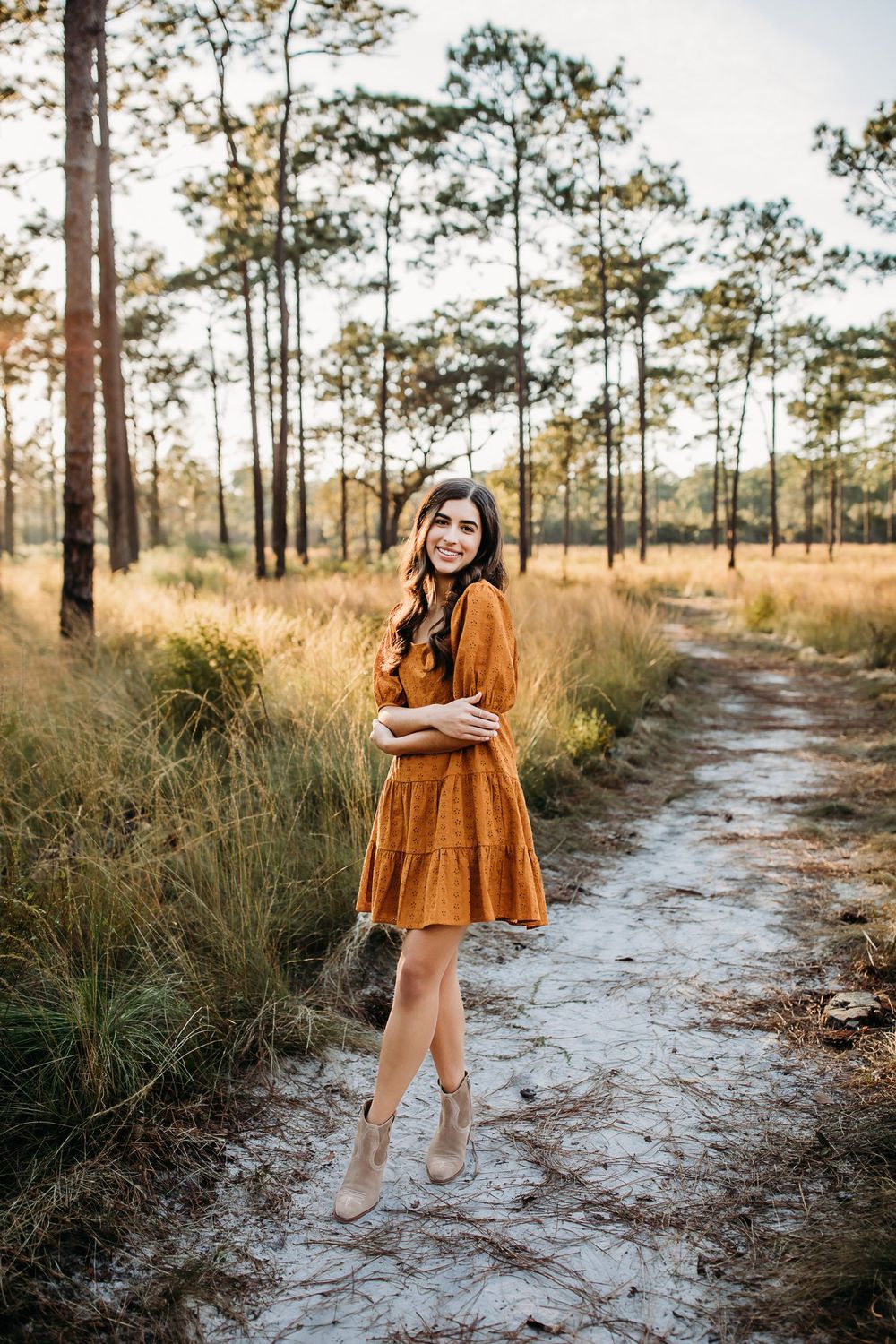 A rustic dirt path winds through tall pine trees and golden grass in a Florida forest on a sunny afternoon.