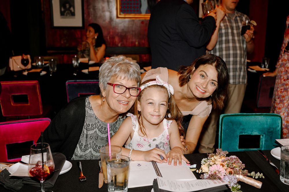A group of people celebrate at a dimly lit restaurant table with drinks and festive decorations.