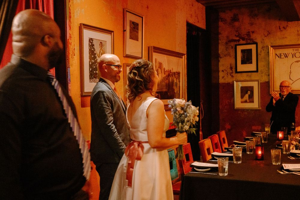 A couple embraces while dancing in an elegantly decorated ballroom with warm lighting and framed artwork.