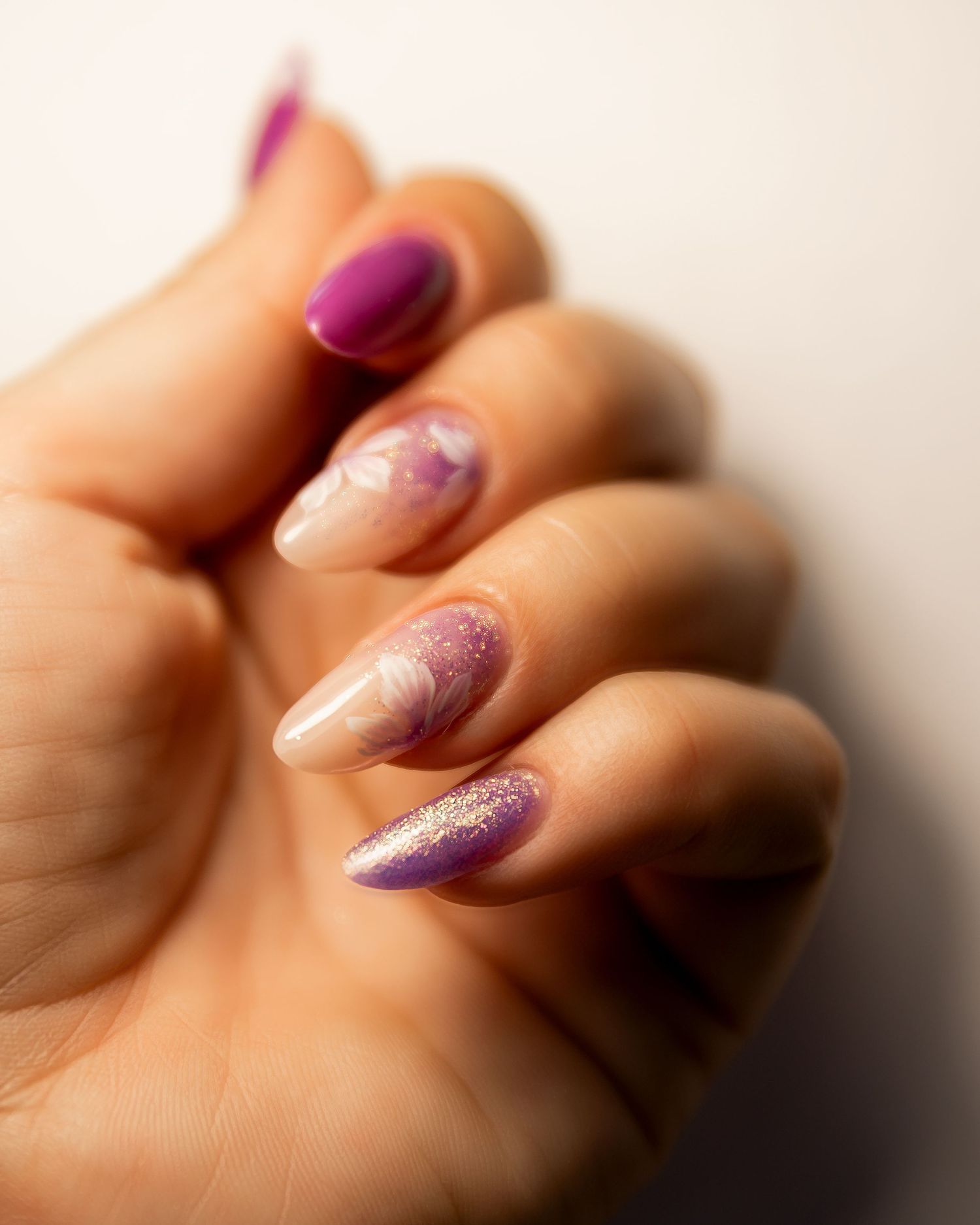 Close up shot of purple glitter gradient manicure on almond shaped nails against soft beige background.