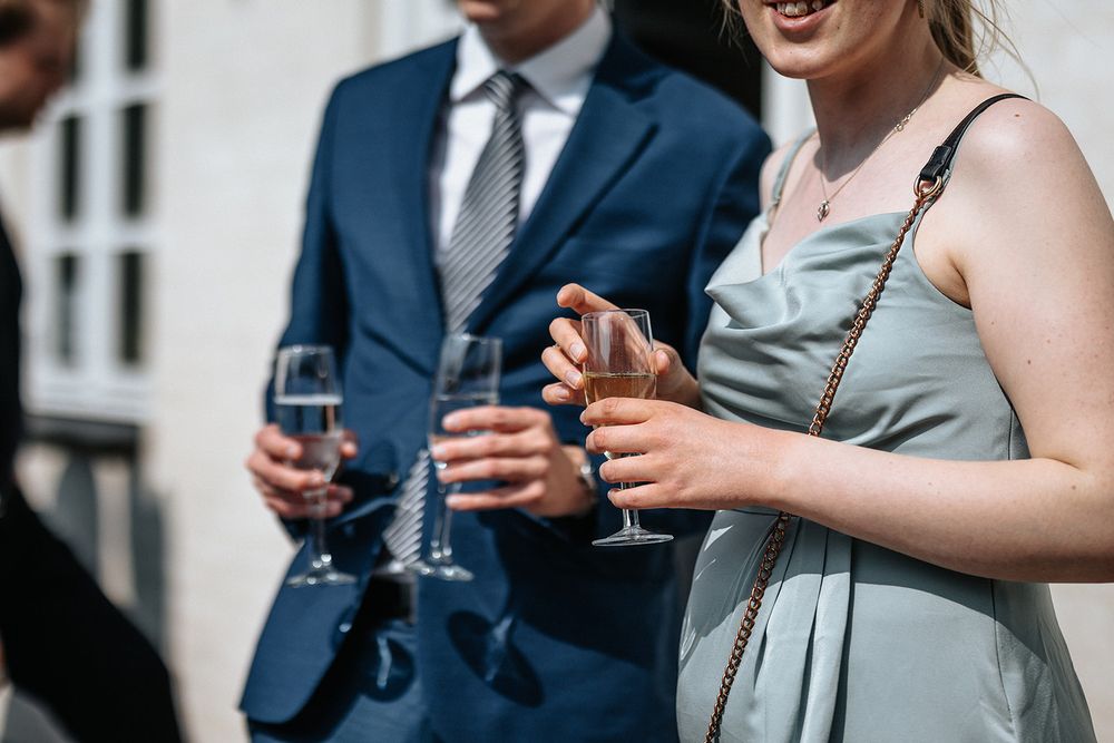 Wedding guests in formal attire clink glasses during an outdoor celebration toast.