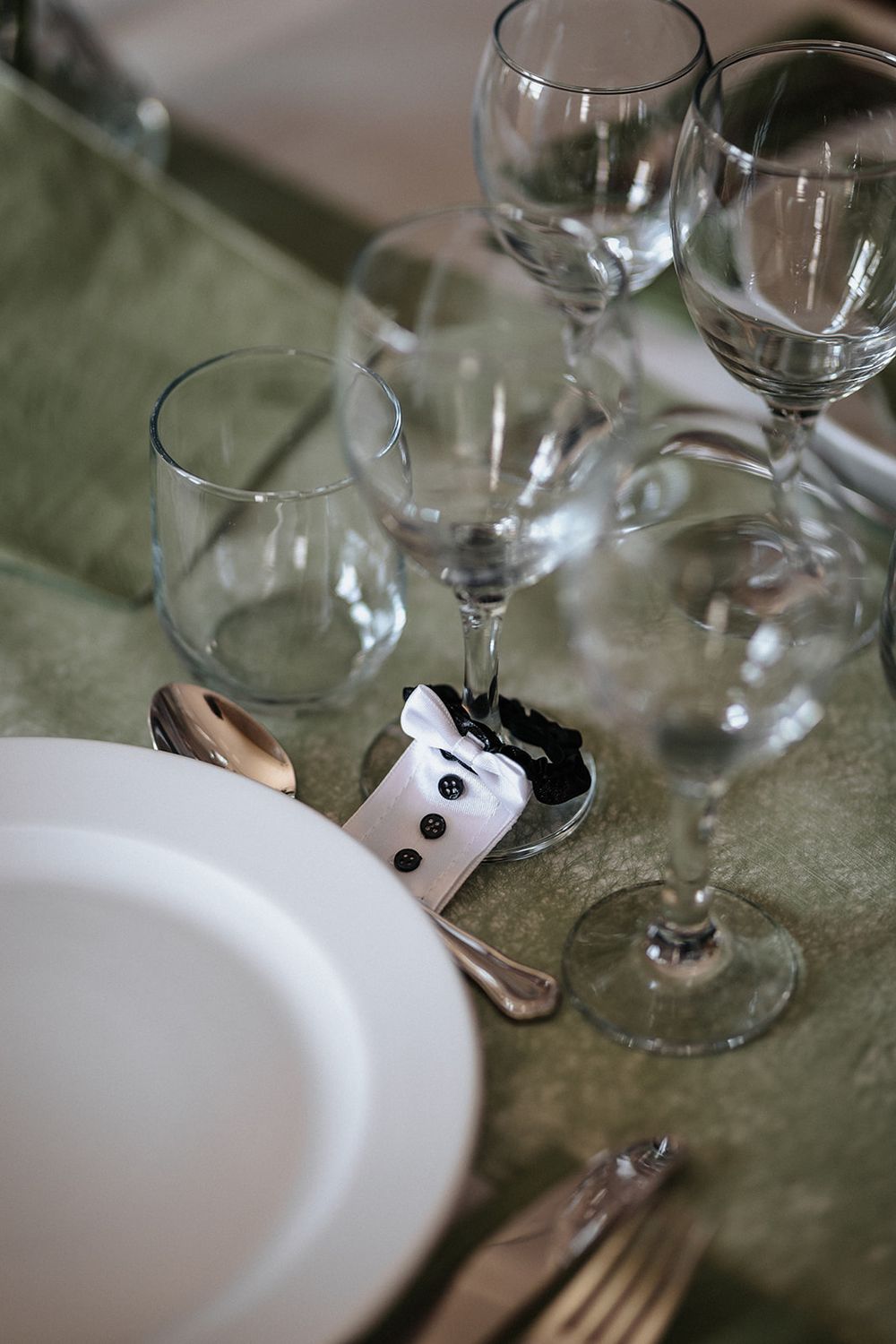 Elegant table setting with wine glasses and white plates on a sage green tablecloth.