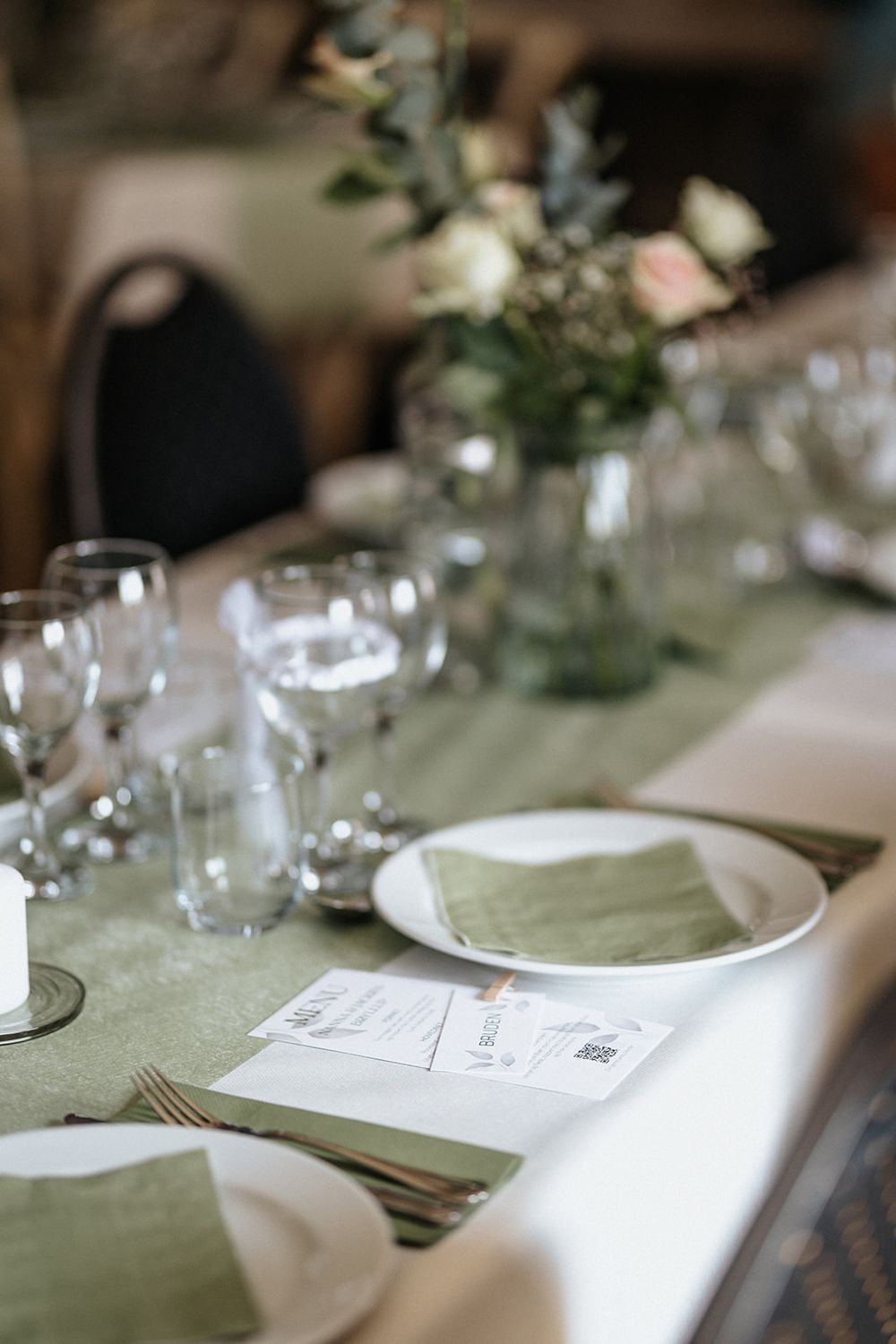 Elegant wedding table settings with white linens, wine glasses and soft green accents create an intimate dining atmosphere.