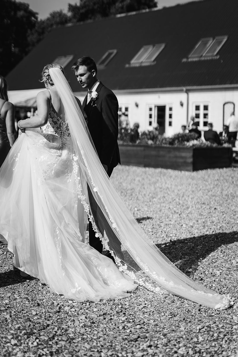 Black and white wedding photo showing a bride's flowing dress train on gravel path.