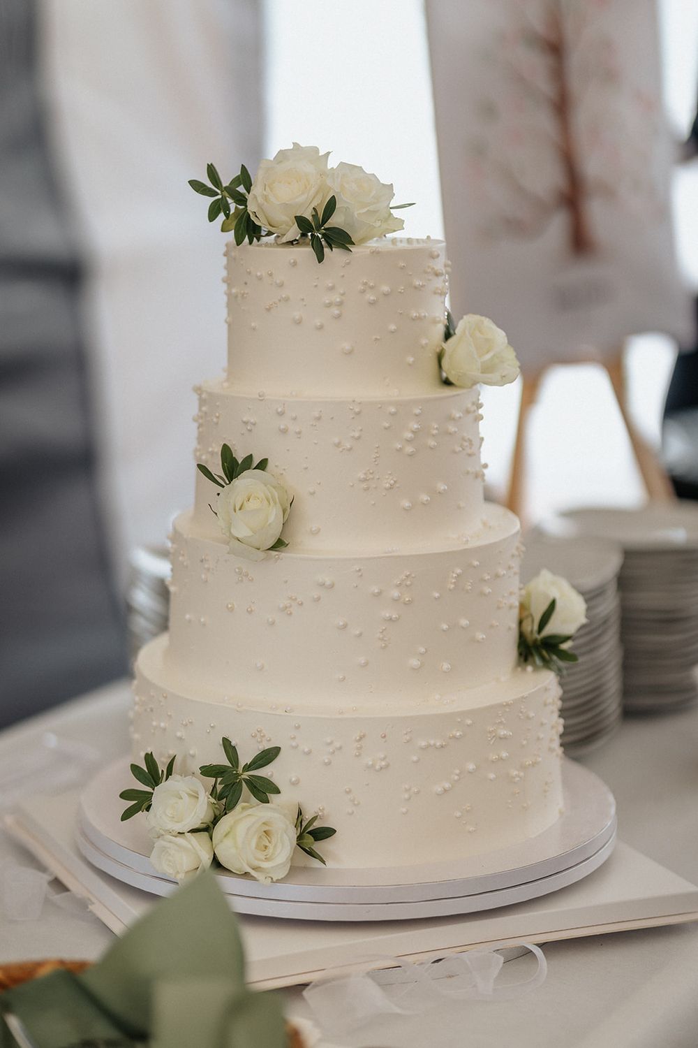 Elegant three-tiered white wedding cake decorated with delicate dots and fresh white roses against a light background.