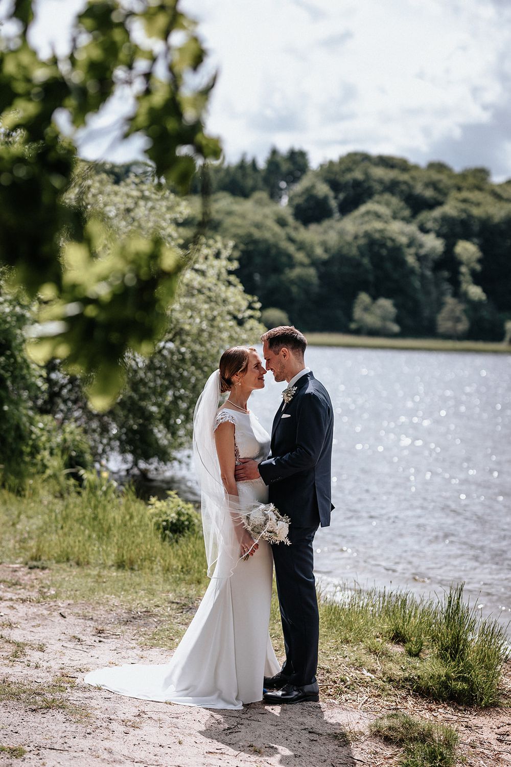 Newlywed couple shares romantic moments by a serene lakeside on their wedding day in a scenic outdoor setting.