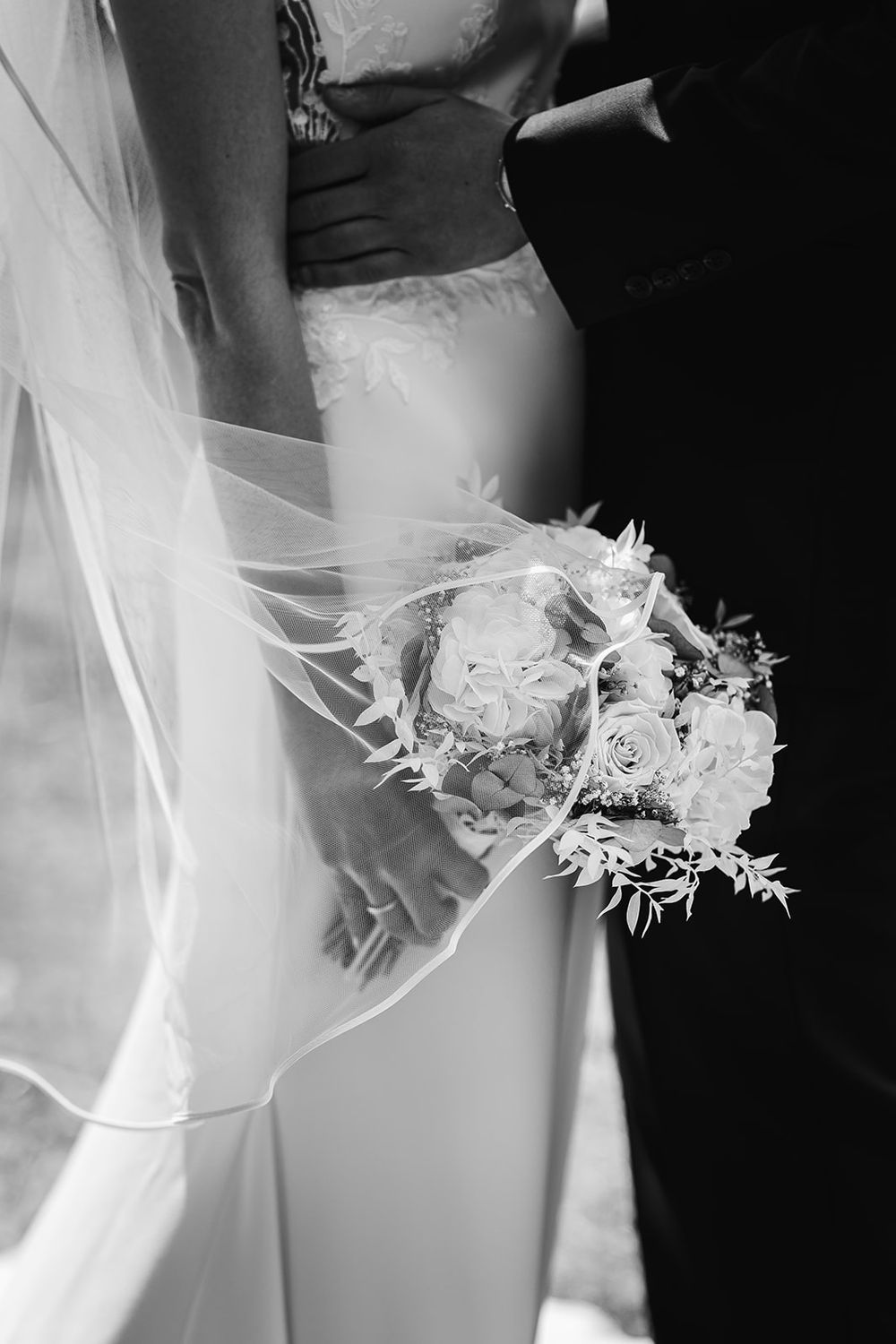 A delicate white bridal bouquet is shown in a series of black and white photographs against a wedding dress.