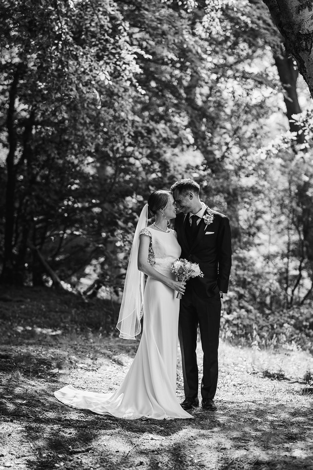 A romantic black and white wedding photo series showing a couple in an intimate outdoor woodland setting.
