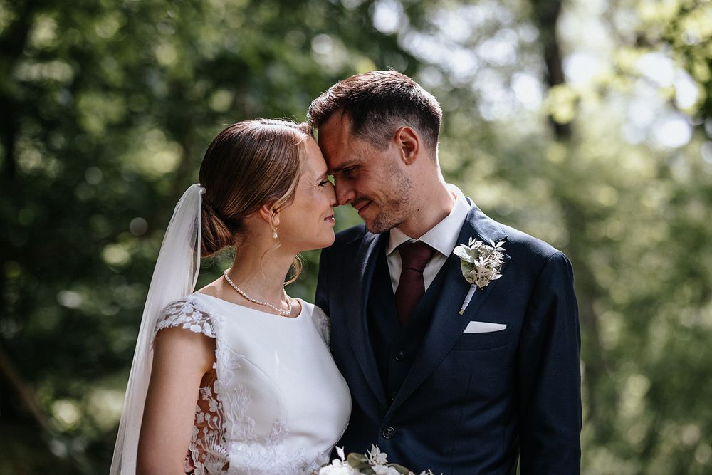 A romantic wedding couple shares an intimate moment in a sunlit garden setting with lush greenery in the background.