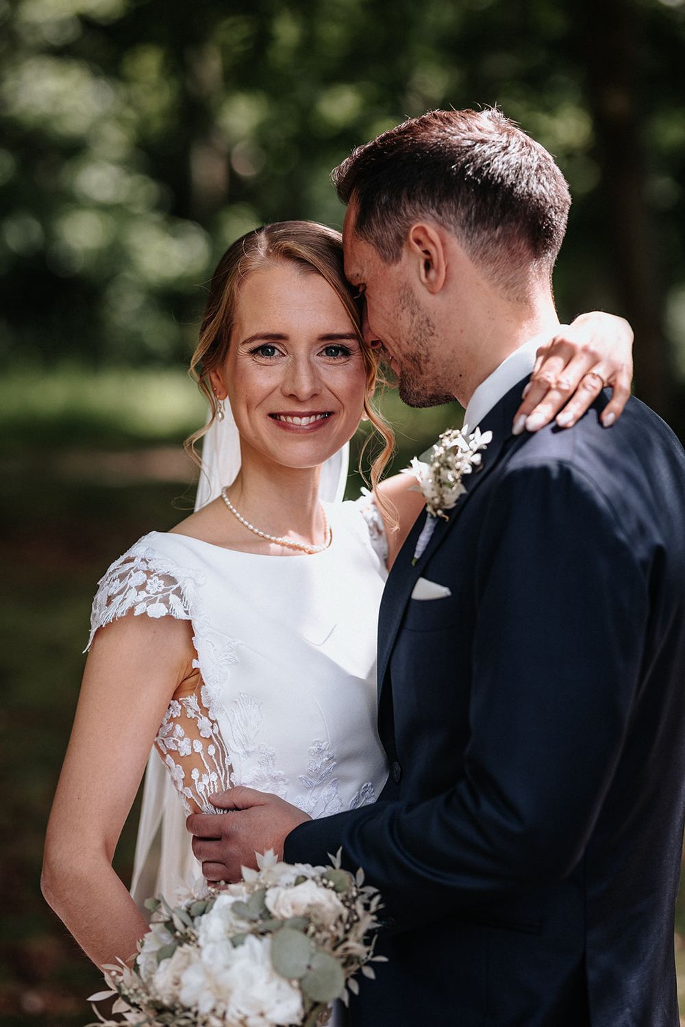 Romantic wedding couple shares intimate moments in outdoor garden setting with white floral bouquet.