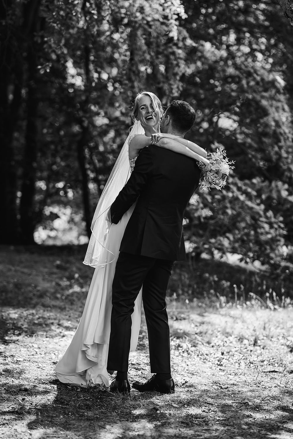 Black and white romantic wedding sequence shows couple embracing in sunlit wooded setting.