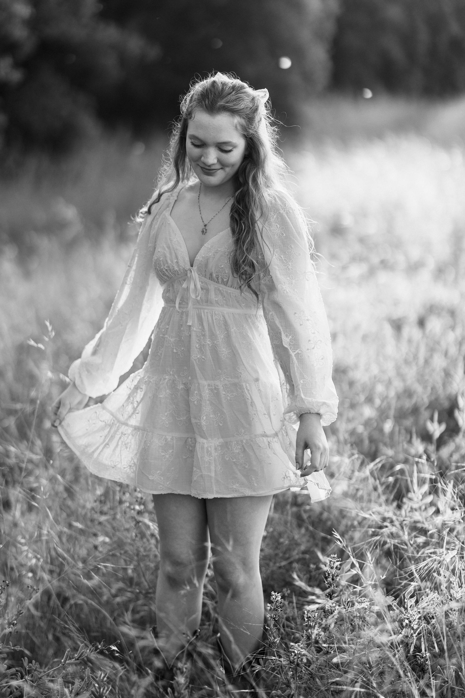 Young girl in white dress twirling through a sunlit meadow in black and white.
