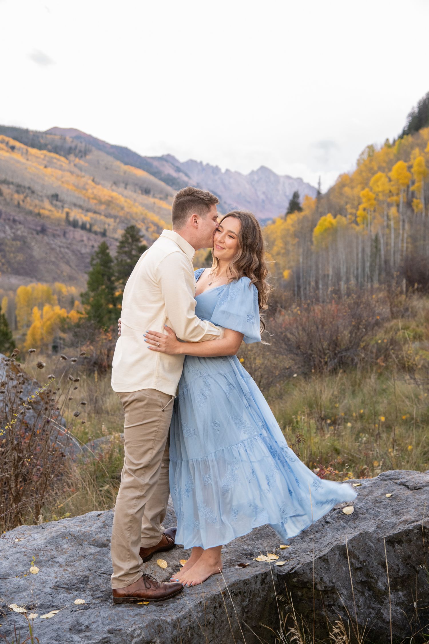 Vail engagement photos in light blue dress and khaki outfit share romantic moments against autumn mountain landscape with golden aspens.
