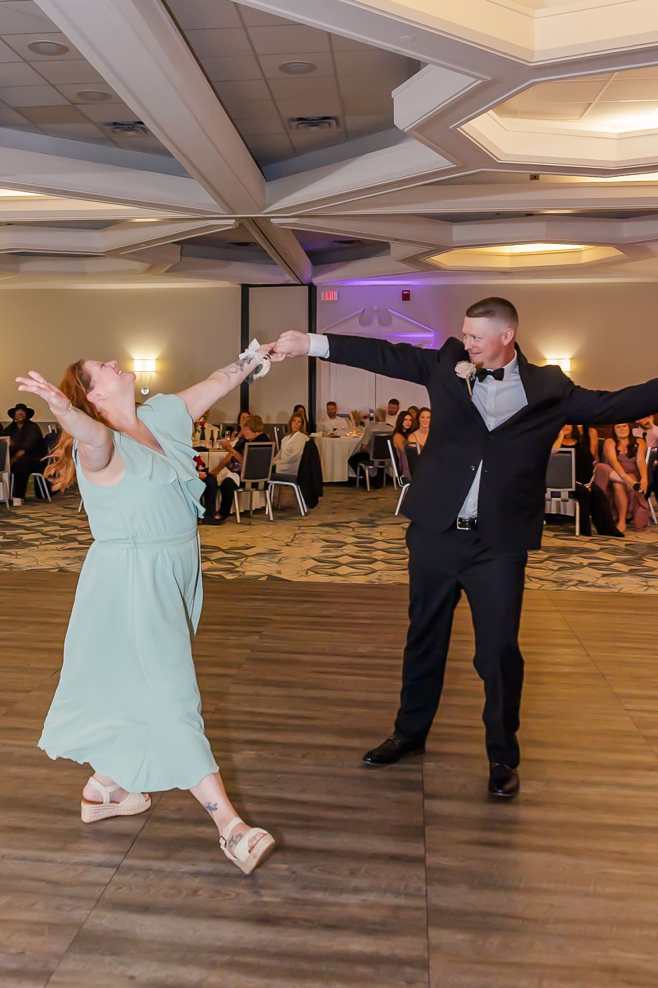 A couple performs a dramatic dip dance move during a wedding reception on a wooden dance floor.