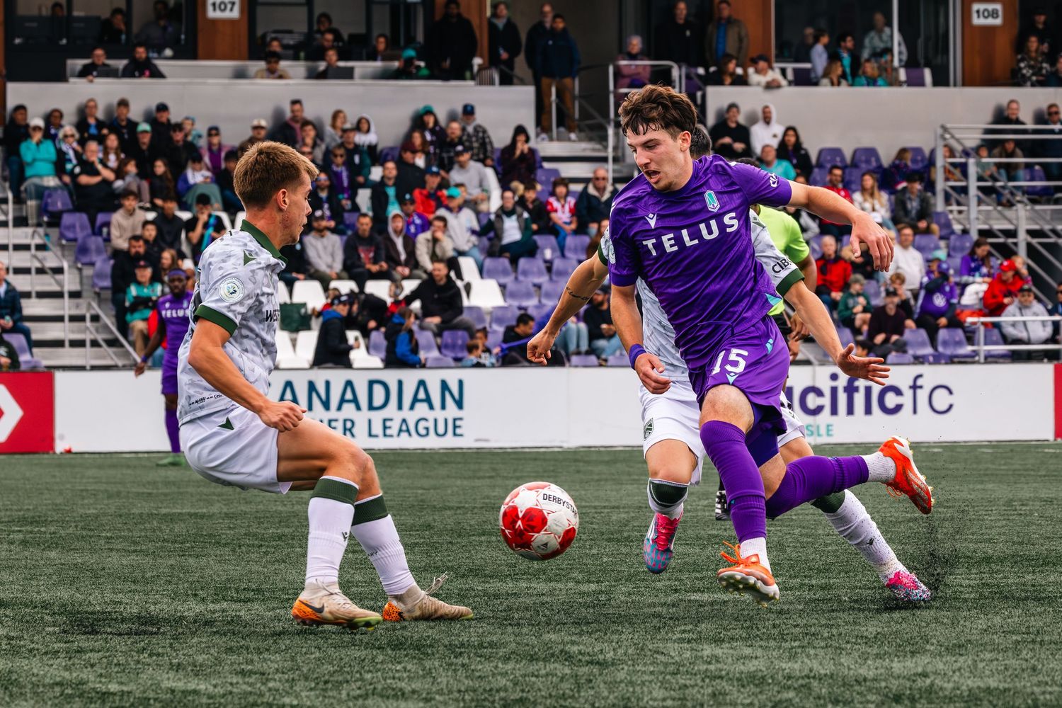 Soccer players from opposing teams in purple and white uniforms jostle for position during a set piece near the goal.