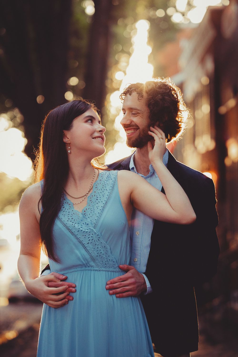 A couple shares a romantic moment at sunset with glowing bokeh lights in the background.