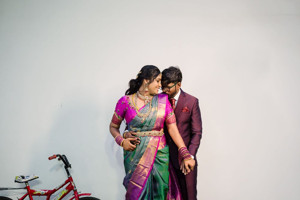 A couple in traditional Indian attire poses for romantic pre-wedding photos with a vintage bicycle in the background.