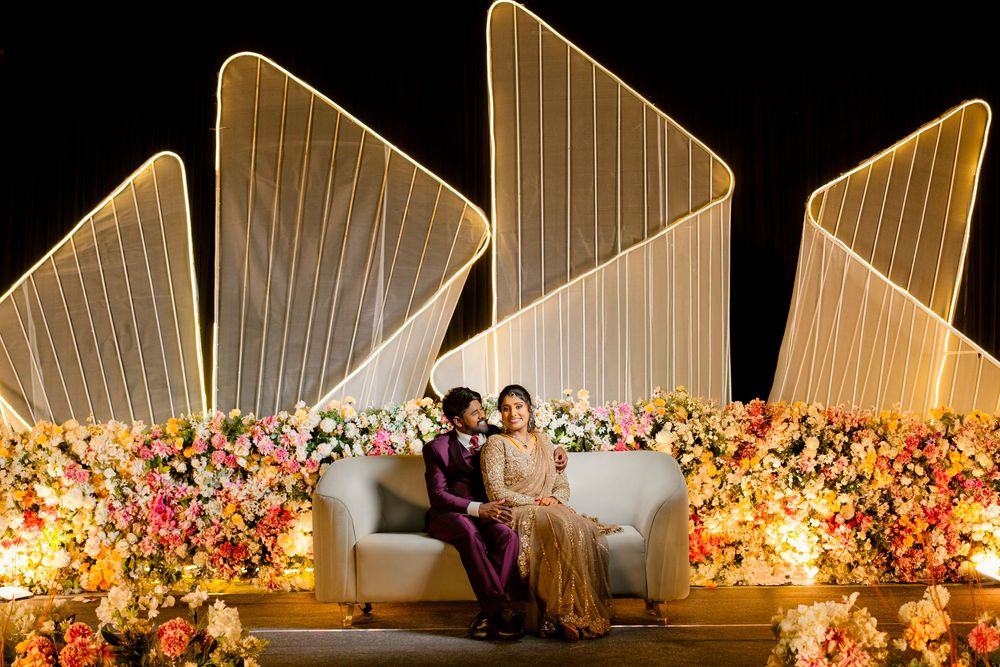 Elegant wedding reception setup with white drapes and vibrant floral arrangements illuminated by warm lighting.