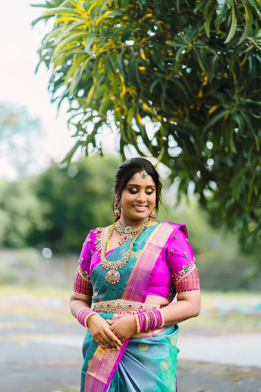 Traditional Indian attire in turquoise and pink with ornate embroidery details photographed in an outdoor garden setting.
