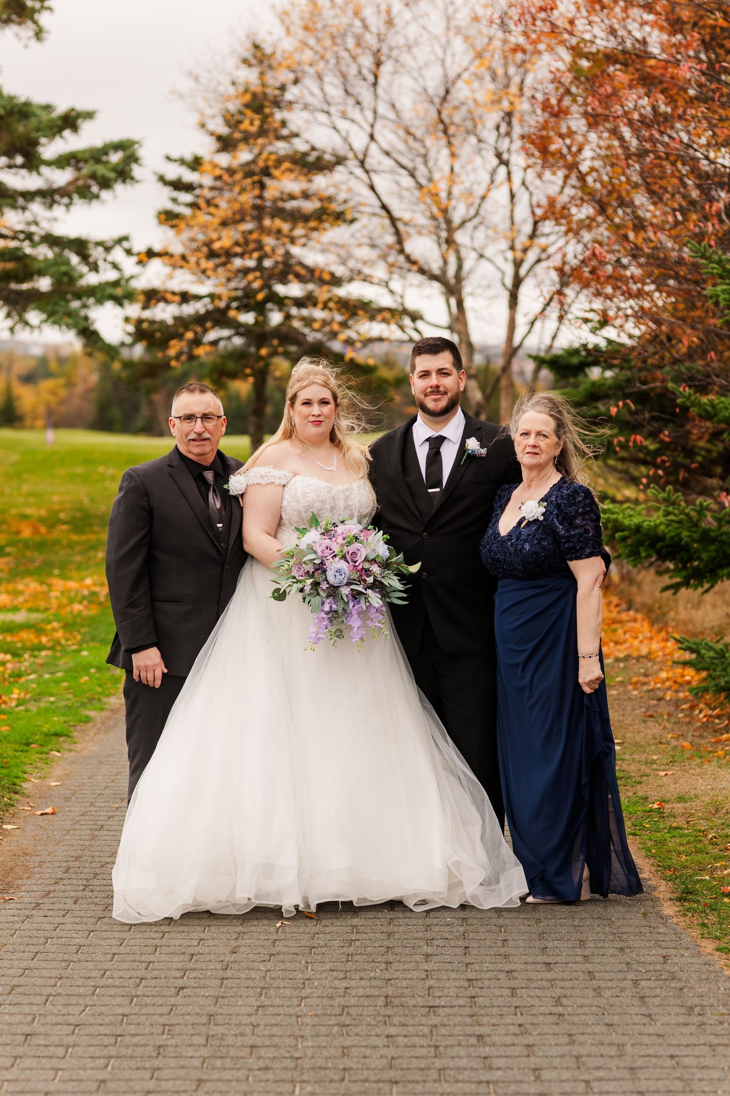 Wedding party poses together on stone pathway surrounded by vibrant autumn foliage in outdoor setting.