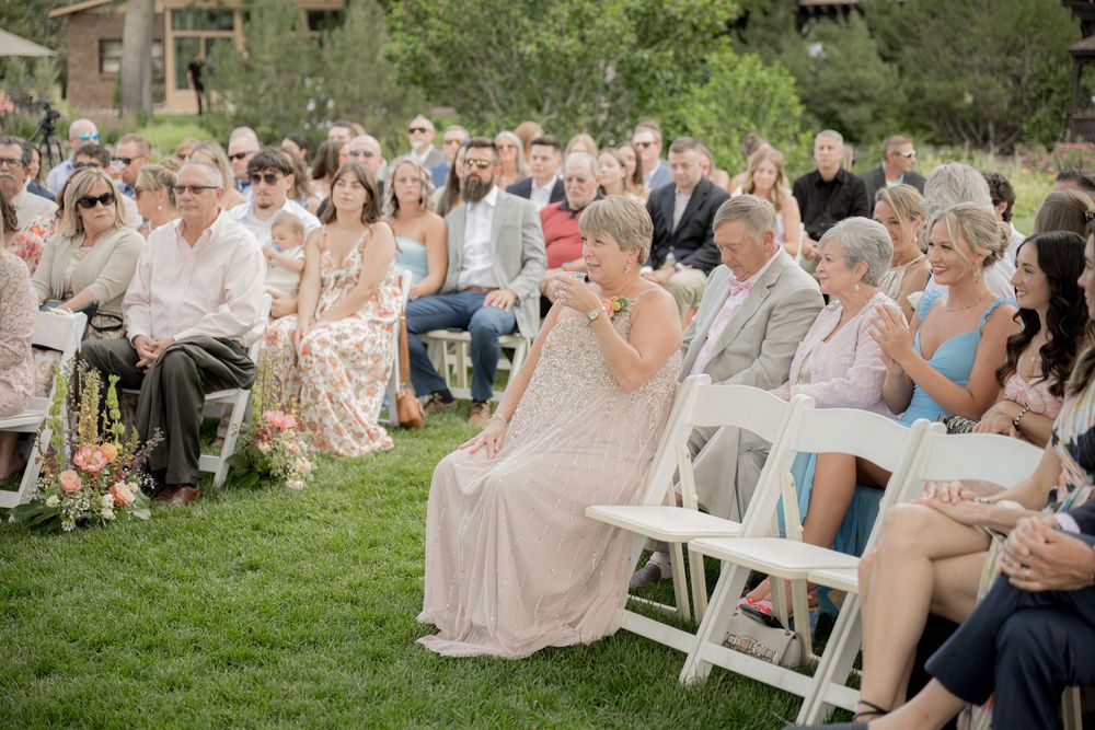 Wedding guests seated in white folding chairs on a lush green lawn during an outdoor ceremony.