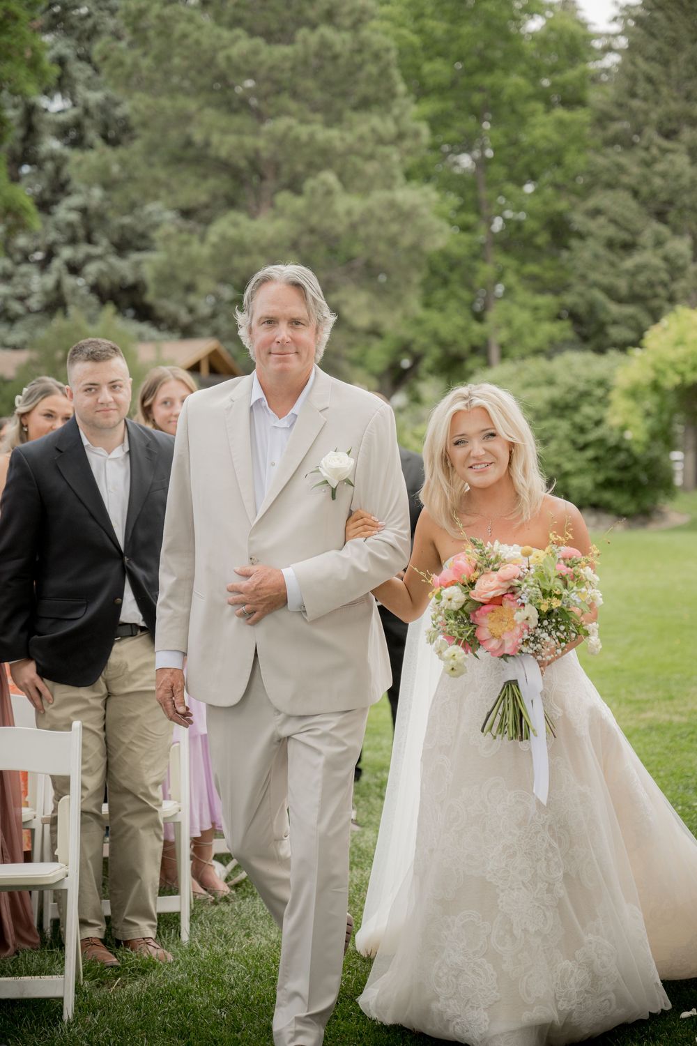Wedding party celebrates outdoors with laughter and joy during summer ceremony on green lawn.