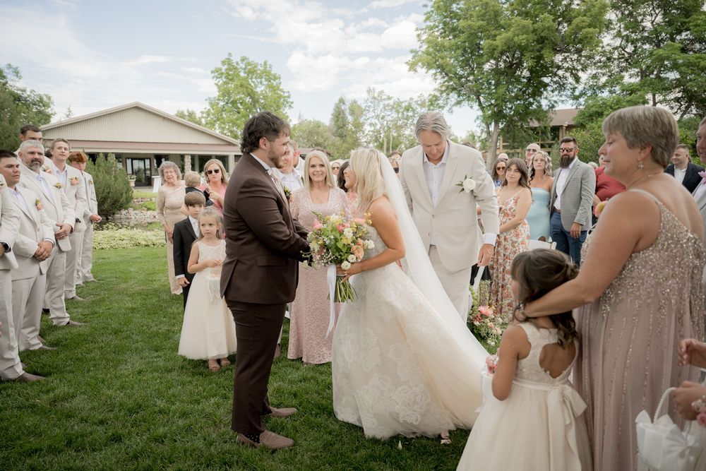 Wedding party gathered on grassy lawn with guests in formal attire celebrating during an outdoor ceremony.