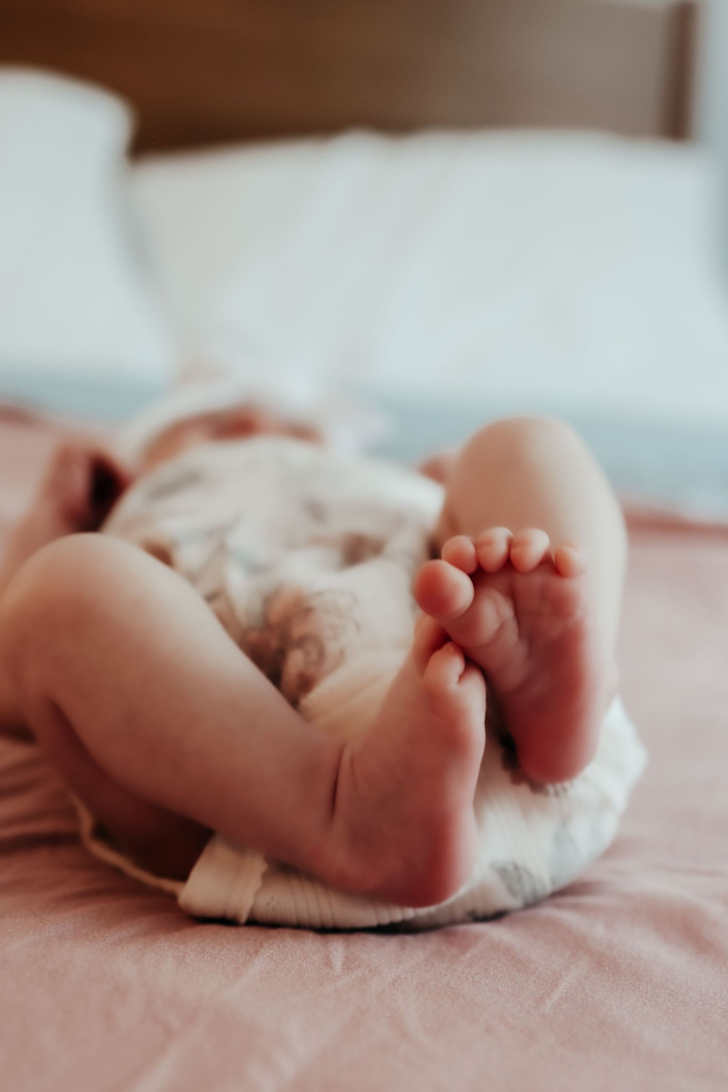 Close-up of tiny baby feet in white cloth diaper resting on pink bedding.