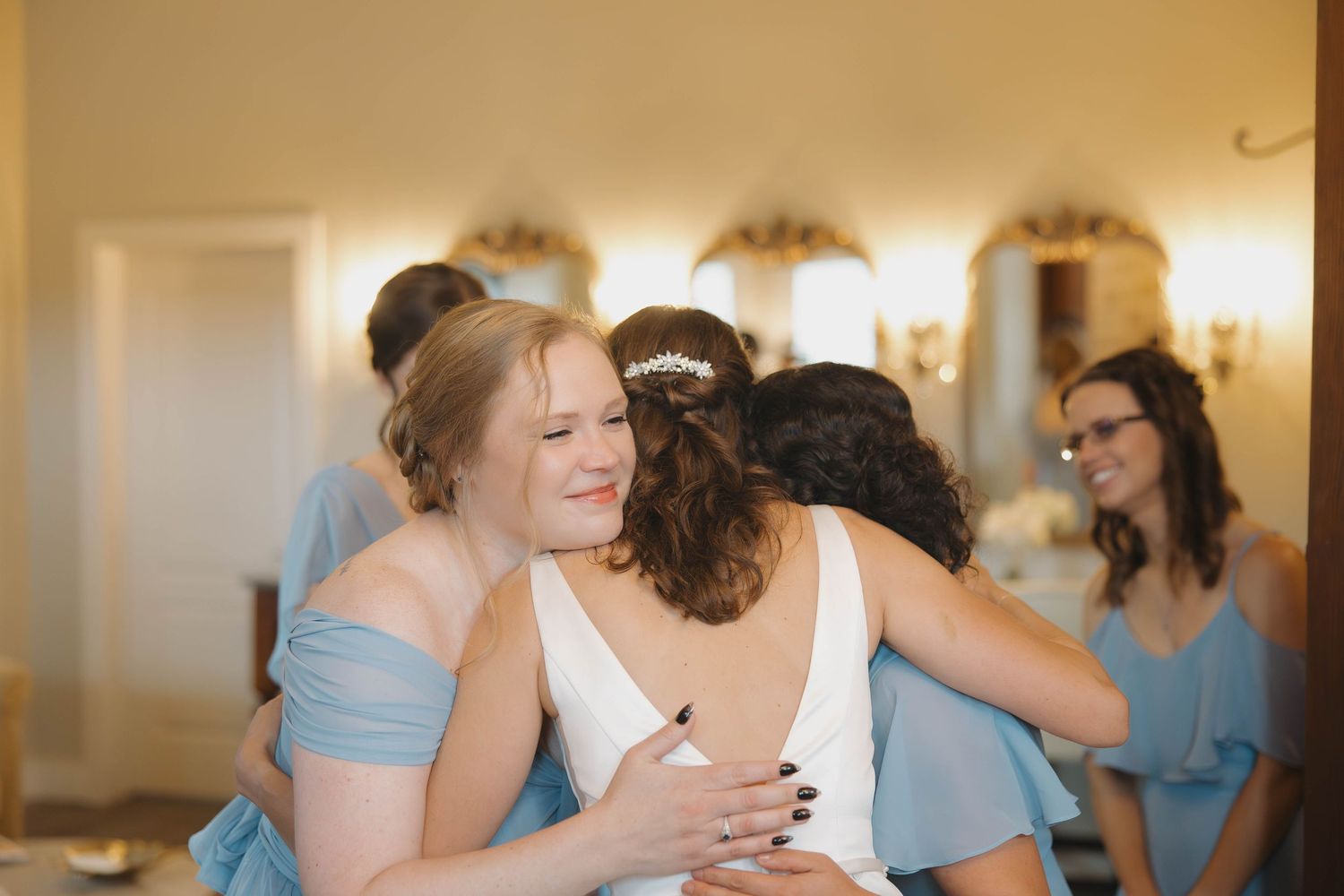 Wedding party members in light blue dresses share emotional embraces during a touching moment at a celebration.
