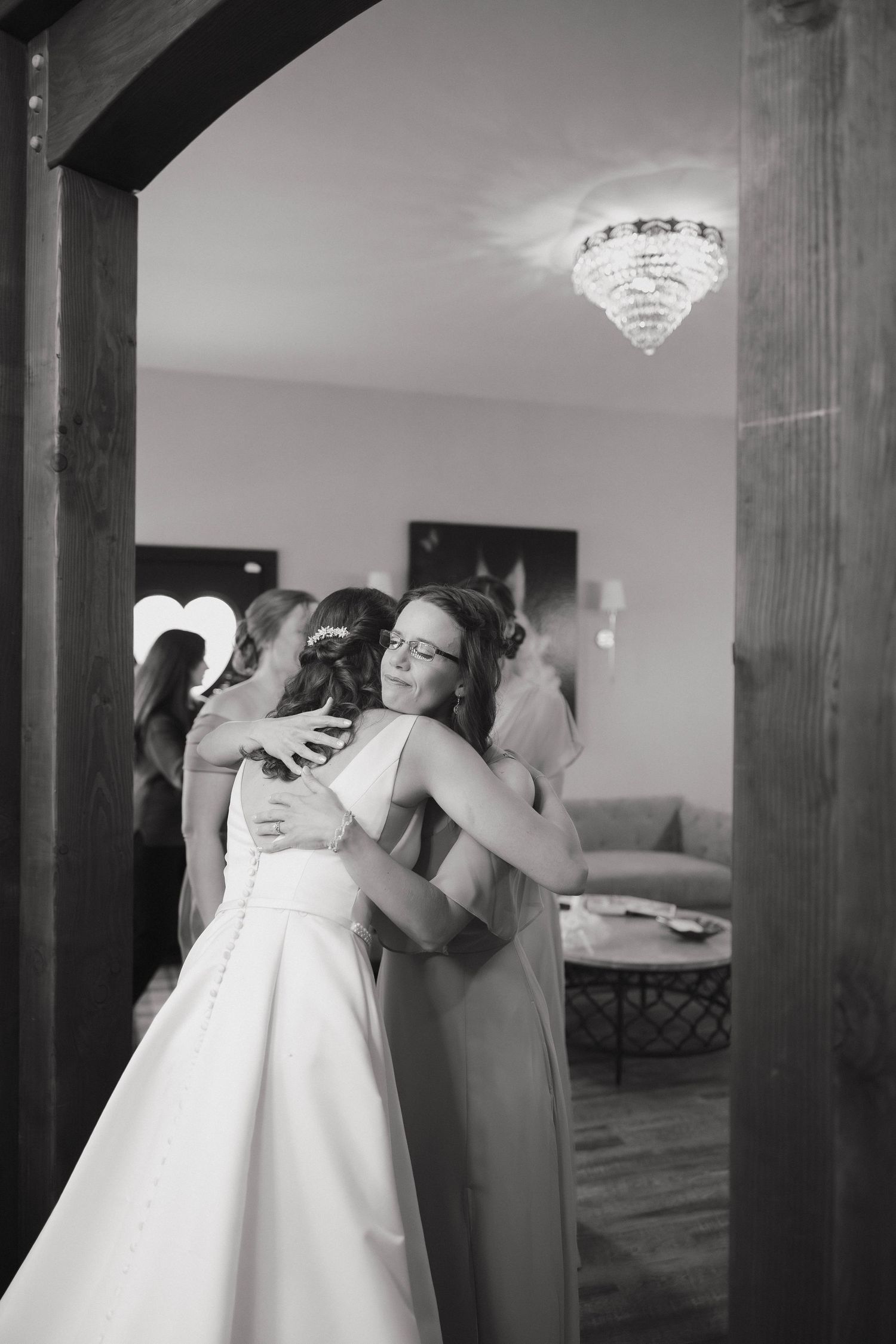 A tender embrace between two people in formal attire at an elegant venue with a crystal chandelier overhead.