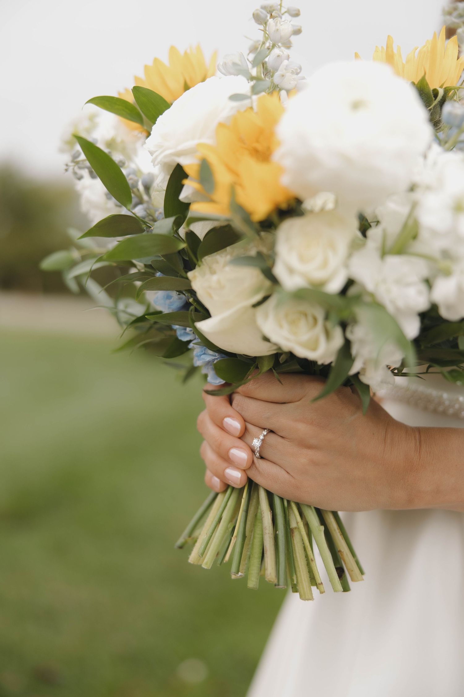 A beautiful wedding bouquet with white roses and yellow flowers held against a blurred outdoor background.